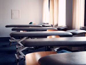 Schwarze Therapieliegen in einer Praxis mit mehreren Behandlungstischen und natürlichem Lichteinfall durch große Fenster.