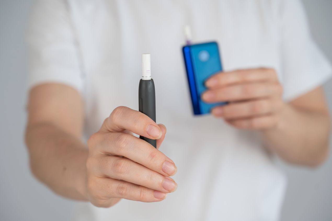 Dampfershop Fokus auf modernes Tabakerhitzer-Geraet in Nahaufnahme mit blauer Powerbank