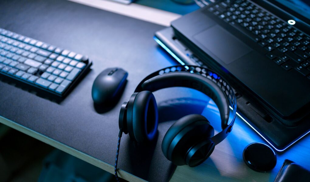 Modernes Gaming-Setup mit Headset, Maus und Laptop auf beleuchtetem Schreibtisch