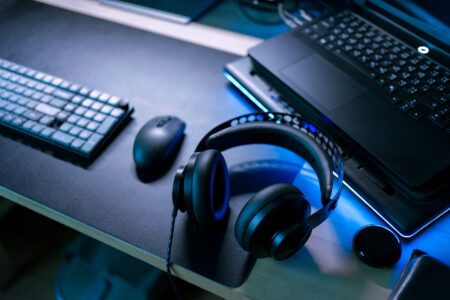 Modernes Gaming-Setup mit Headset, Maus und Laptop auf beleuchtetem Schreibtisch