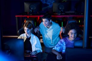 Drei junge Gamer spielen zusammen an PCs und erleben gemeinsames Multiplayer-Gaming