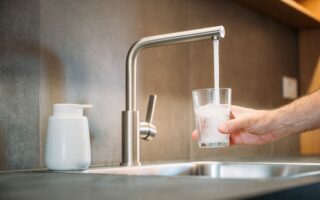 Glas wird mit klarem Wasser aus modernem Küchenhahn gefüllt – Symbol für sauberes Trinkwasser durch Osmose Filteranlage
